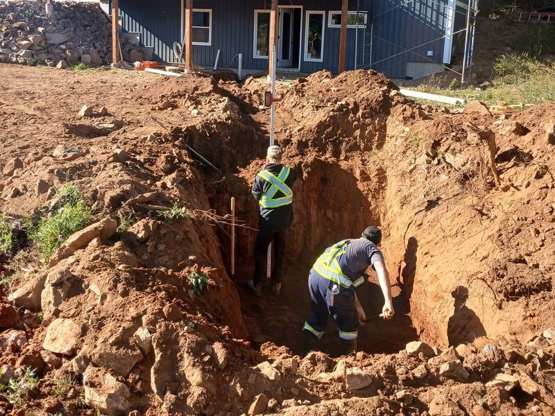 Two crew members working in a deep excavation on a septic install