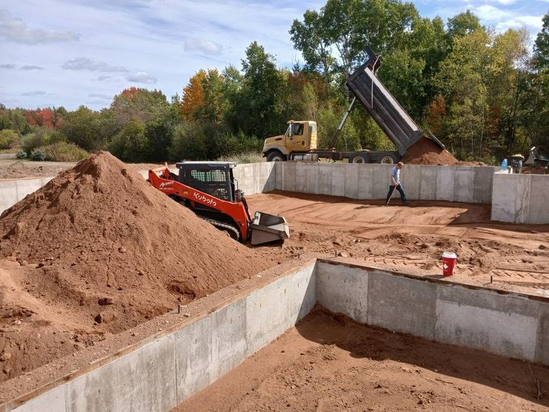 Skid steer and dump truck backfilling a newly poured concrete foundation