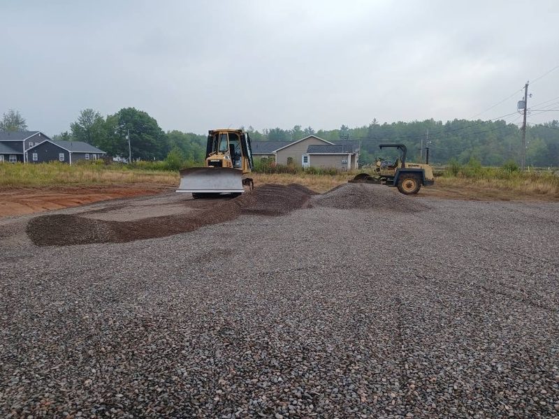 Loader and roller spreading crushed gravel across a new parking area