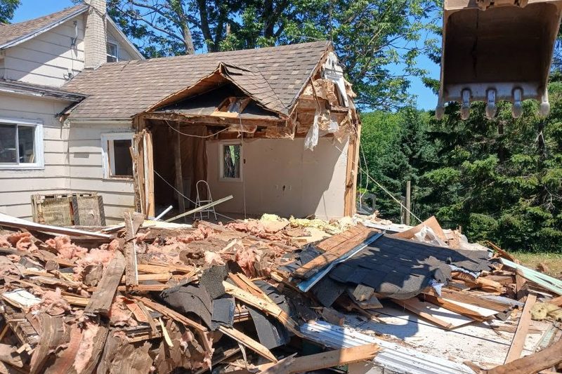 Excavator bucket tearing down a house addition with debris piled below