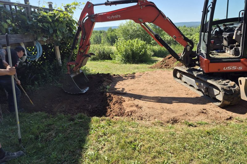 Mini excavator opening a backyard dig with a crew member guiding the cut