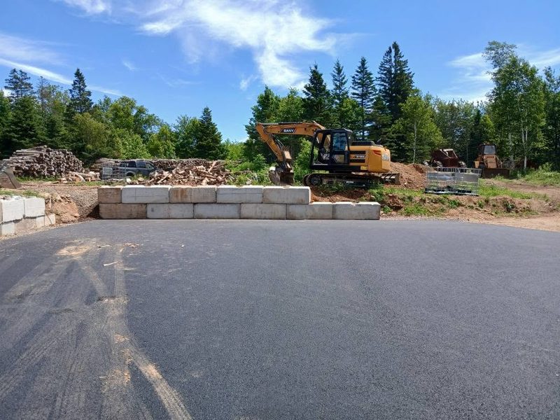 Excavator placing concrete lock blocks for a retaining wall beside fresh asphalt
