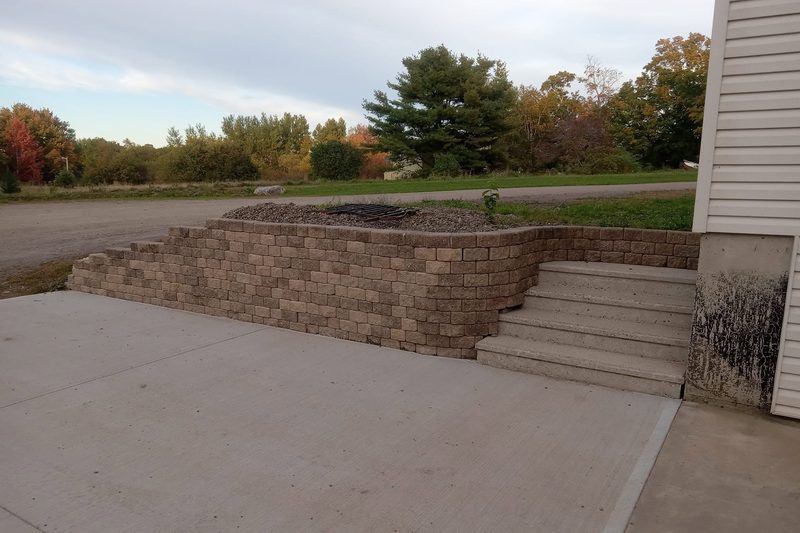 Finished block retaining wall with steps beside a new concrete pad