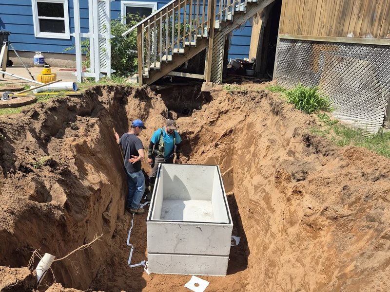 Concrete septic tank being set into an excavated pit by the crew